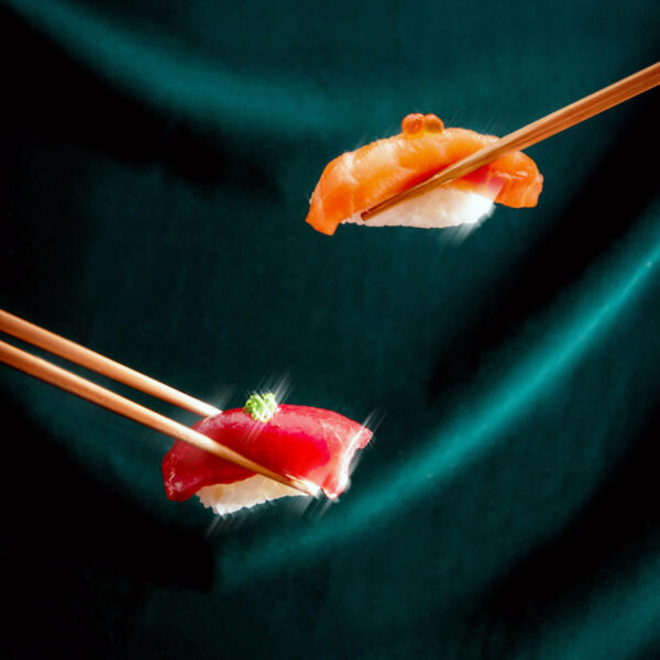 Two sets of chopsticks holding sushi against a green velvet backdrop at Aera restaurant in Toronto