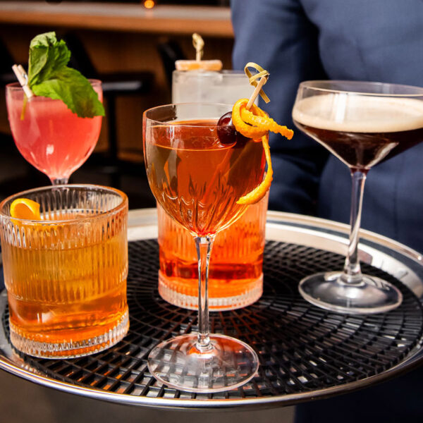 six colourful cocktails on a serving tray held by a server in a suit