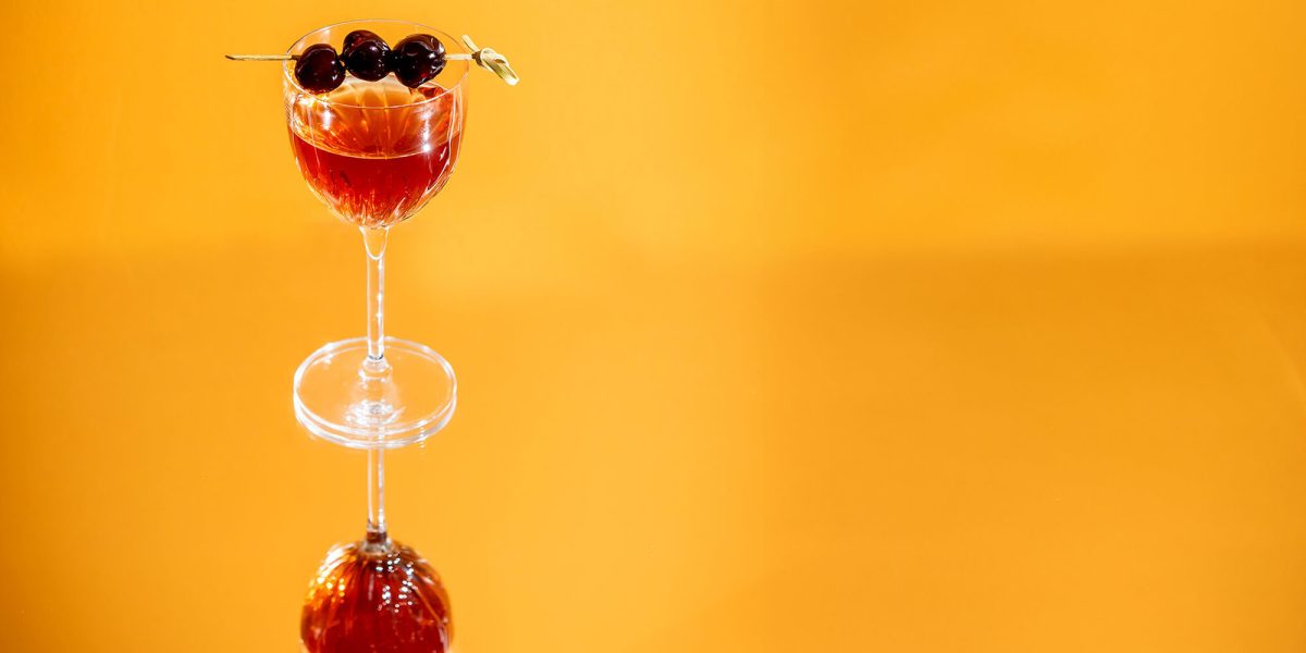 cocktail garnished with cherries against a gold backdrop at Aera Restaurant in Toronto